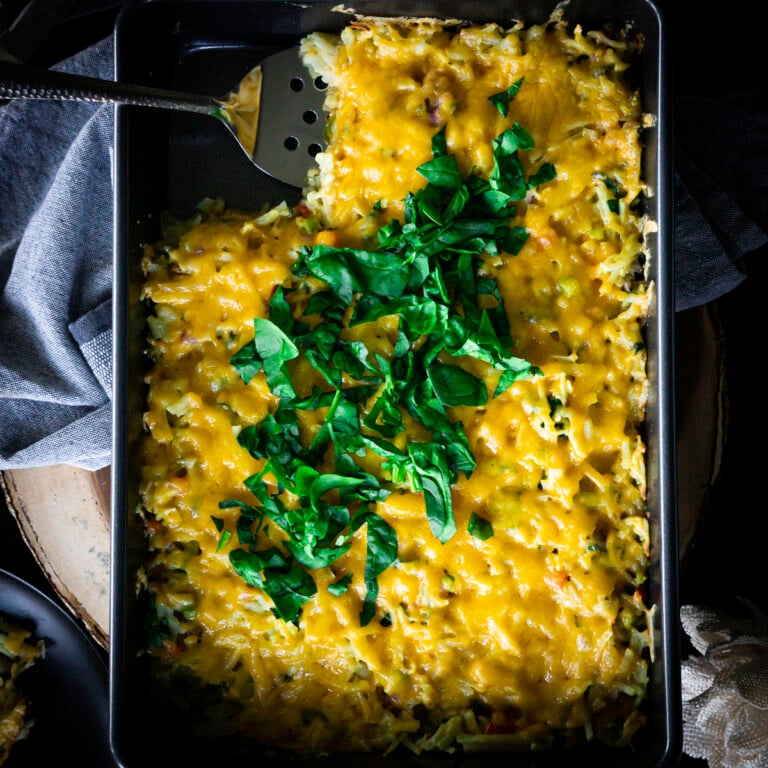 Full hashbrown casserole dish topped with fresh spinach and cheese