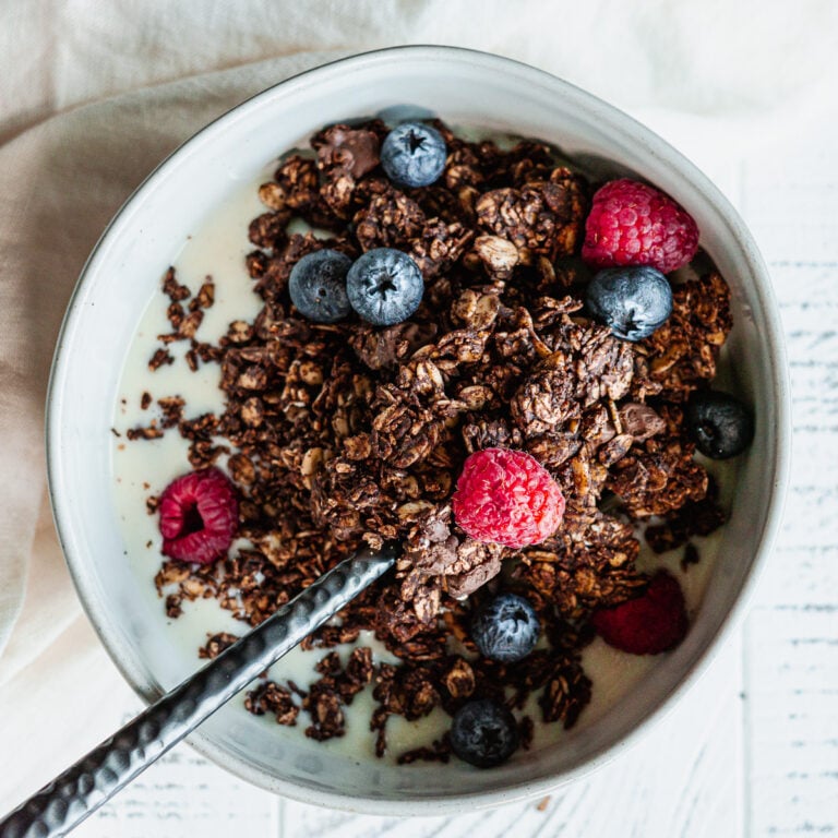 Dark chocolate granola in a bowl with soy milk and fresh fruit