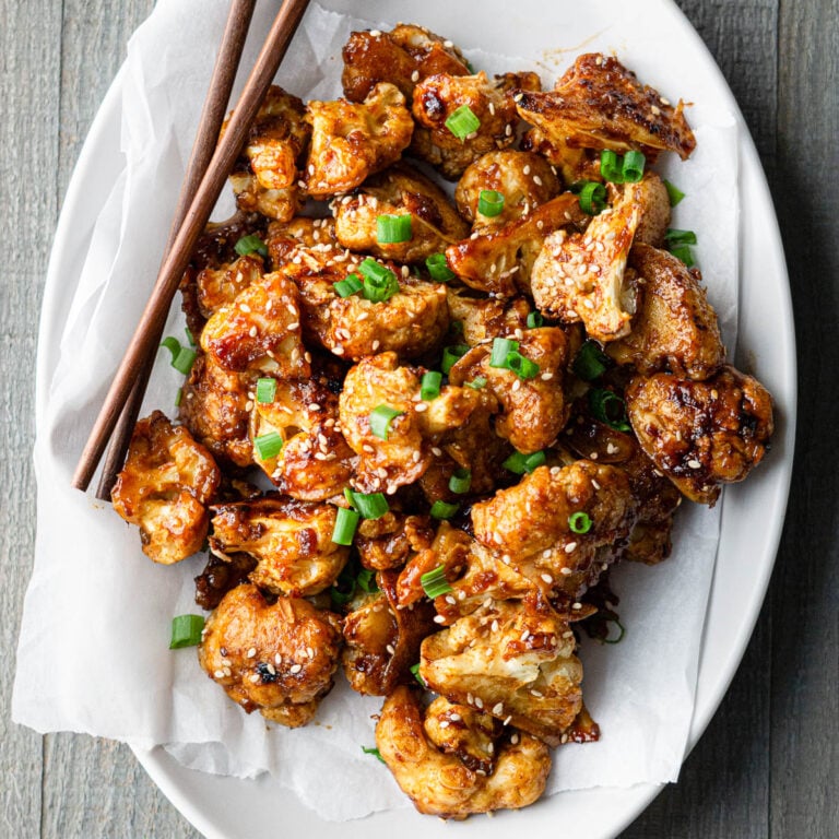 Gochujang Cauliflower wings garnished with sesame seeds and green onions and served with chopsticks