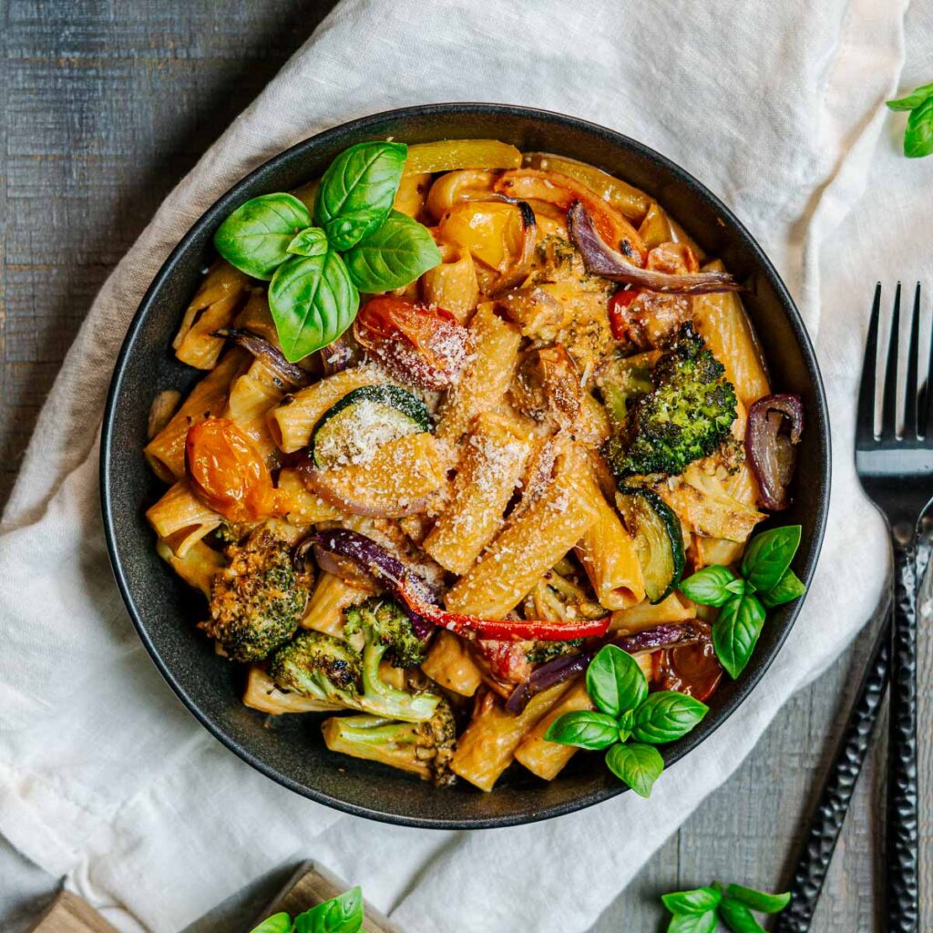 pasta with roasted vegetables in a serving bowl garnished with basil