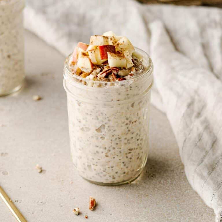 mason jar filled with overnight oats topped with apples, pecans, and cinnamon